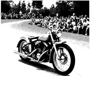 A vintage bike with a classic design is racing along a dirt track. The bike has a shiny metal frame and distinct features that highlight its retro style. In the background, a crowd of spectators is visible, with some standing and others sitting on the ground, all of them enthusiastically cheering. The dirt track is surrounded by grass, and there are trees lining the edges, adding to the setting. The atmosphere captures the excitement of the race as the bike speeds ahead.