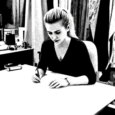 A woman with blonde hair styled in a sleek ponytail is sitting at a large drafting table. She is intently sketching designs for new outfits on a sheet of paper. The drafting table is cluttered with various fabric swatches in different textures and patterns, neatly arranged around her. A pencil is held in her right hand, poised to add details to her design. The scene conveys a sense of creativity and fashion design, with the surrounding fabrics offering a vibrant backdrop for her artistic process.