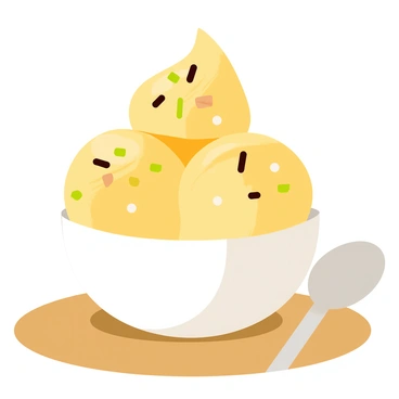 A white ceramic cup filled with creamy yellow jackfruit ice cream. The ice cream has a smooth texture and is topped with a generous sprinkle of chopped nuts, such as almonds and pistachios. The cup is placed on a wooden table, and a small silver spoon rests beside it.