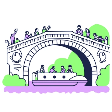 A barge is gliding smoothly beneath a historic stone bridge. The bridge features intricate carvings and arches that showcase its architectural significance. Tourists are gathered on the bridge, capturing photographs with their smartphones. Some individuals are leaning over the edge, while others are standing in groups. The scenery around the bridge includes lush greenery and a clear sky, adding to the picturesque view. The water below reflects the structure of the bridge and the passing barge.