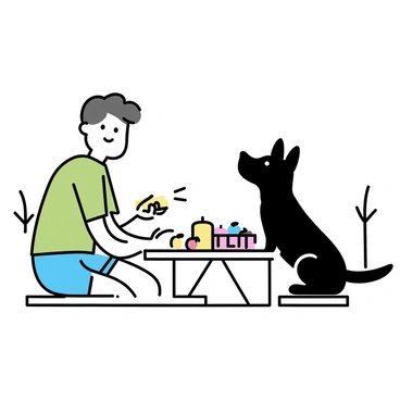 A black dog sitting on a wooden picnic table. The dog is looking up at a person sitting across from it. The owner, wearing a green t-shirt and denim shorts, is smiling and holding a sandwich. There is a picnic basket on the table, alongside a few colorful fruits. The scene is set in a grassy area with a few trees in the background.