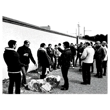 A group of people is gathered near the Berlin Wall as it is being demolished. Some individuals are reaching out to collect fragments of the wall, eagerly holding pieces of concrete in their hands. A man with a camera is capturing the moment, while another person is carefully inspecting a larger piece of the wall. The scene captures a mix of emotions, from excitement to nostalgia, as the crowd interacts in front of the crumbling structure. In the background, there are remnants of the wall still standing, and the atmosphere is filled with a sense of history being made.