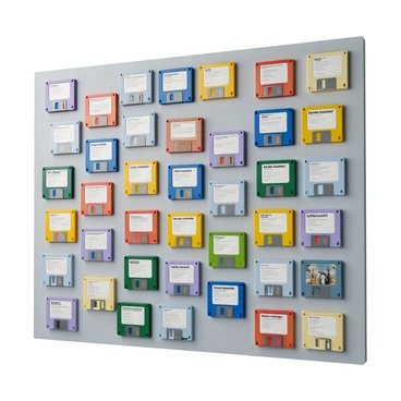 A wall display featuring an arrangement of colorful floppy disks, each displaying distinct DOS software labels. The disks are positioned in a mosaic pattern, showcasing a variety of vibrant colors including bright red, blue, green, and yellow. The labels on the disks are in different fonts and sizes, clearly indicating various software titles. The background is a neutral shade to enhance the visual impact of the colorful disks. The display creates a retro technological aesthetic, reminiscent of the late 20th century.
