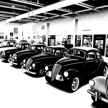 A vintage car showroom features an array of classic cars from the 1950s. The space is filled with several distinct models, showcasing their unique shapes and chrome details. Each car has polished surfaces reflecting light, emphasizing their elegant curves and designs. The showroom has neatly arranged displays, with some cars parked side by side, while others are positioned at angles to highlight their features. The floor is shiny and well-maintained, contributing to the overall nostalgic ambiance. Various memorabilia from the 1950s adorns the walls, creating a connection to the era.