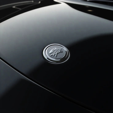 A luxury car emblem prominently displayed on the hood of a sleek, polished black vehicle. The emblem features intricate details, showcasing a stylized logo engraved in chrome with a reflective surface catching the light. Surrounding the emblem, the smooth contours of the car’s hood exhibit a high-gloss finish, enhancing the upscale aesthetics of the vehicle. The background includes a subtle play of light and shadow, emphasizing the emblem's sophistication and craftsmanship.