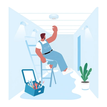 A person with short hair is climbing a ladder to reach a smoke detector mounted on the ceiling. The person is wearing a utility belt that holds various tools. A tool kit is positioned at the base of the ladder, filled with pliers, a screwdriver, and other equipment. The hallway is bright, featuring walls painted in a soft pastel color, and there are light fixtures installed along the ceiling that provide ample illumination. A small potted plant sits in a corner of the hallway, adding a touch of greenery to the scene.