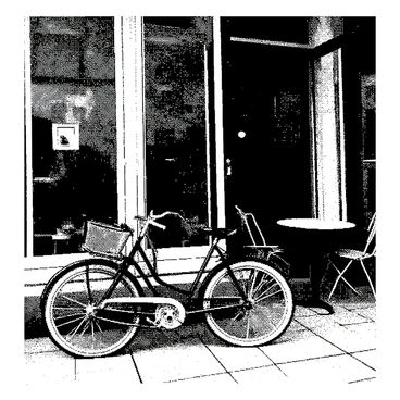 A vintage bike is parked against the wall of a cozy corner bistro. The bike has a classic design with a shiny frame and a leather seat. The bistro features a small round table with two chairs, positioned on a checkerboard-patterned floor. The bistro's entrance is framed by large glass windows, showcasing a welcoming atmosphere inside. There are potted plants placed on the windowsill, adding a touch of greenery to the scene. The overall setting exudes a charming, quaint vibe.