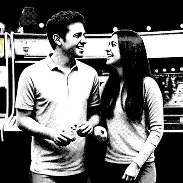 A couple is standing together in an arcade, surrounded by colorful game machines. The man has short dark hair and is wearing a casual shirt. The woman has long, wavy hair and is dressed in a light sweater. They are both smiling and looking at each other, sharing a moment of joy. The game machines are brightly lit, displaying various classic arcade games. In the background, other players can be seen engaged in different games, adding to the lively atmosphere of the arcade. The couple is holding a few game tokens in their hands, ready to play.