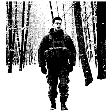 A soldier is standing upright in a snowy forest, wearing a winter camouflage uniform. The uniform is designed with a pattern that blends into the snowy surroundings. Snowflakes are gently falling around the soldier, covering the ground and branches of the trees nearby. The soldier has short, dark hair and a focused expression, with their eyes scanning the environment. The trees in the background are tall and covered in white snow, creating a stark contrast against the dark uniform. The scene conveys a sense of stillness and vigilance.