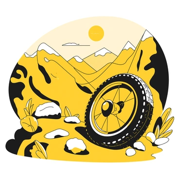 A bike tire resting on a rugged section of an alpine trail, surrounded by rocky terrain and patches of grass. The tire is black, with a textured surface, and is positioned in the foreground. In the background, expansive valley views stretch out beneath a clear sky, showcasing layers of distant mountains and steep cliffs. The scene is illuminated by sunlight, casting defined shadows from the tire onto the trail.