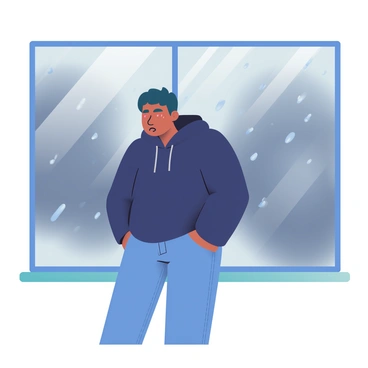 A person with medium skin and short black hair is standing in front of a large window during a rainstorm. They are wearing a dark blue hoodie and jeans. The window is covered with droplets of rain, creating a blurred effect on the outside view. The person's reflection is visible in the glass, showing a worried expression with furrowed brows and slightly parted lips. The background outside the window features dark gray clouds and streaks of rain falling, enhancing the somber mood of the scene.