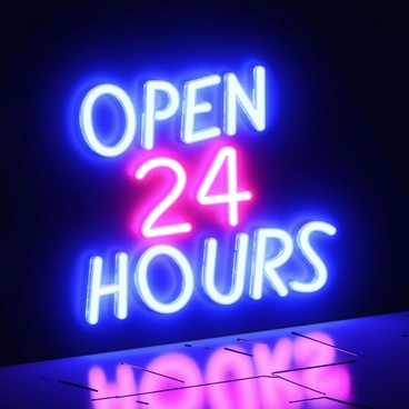 A neon sign with the words "Open 24 Hours" glowing in bright blue and pink hues. The neon light emits vibrant rays that bleed into the surrounding darkness, creating a soft halo effect. The dark background highlights the intensity of the colors, while faint reflections shimmer on a nearby surface.