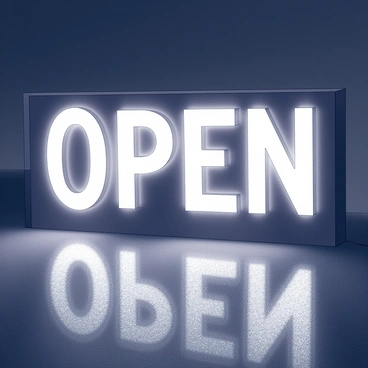 A glowing sign spelling "open" is prominently displayed. The letters are bold and stylized, with a luminescent effect that radiates from the edges. The sign is set against a dark background, enhancing its brightness. The surrounding area is dimly lit, creating a stark contrast that draws attention to the illuminated text.