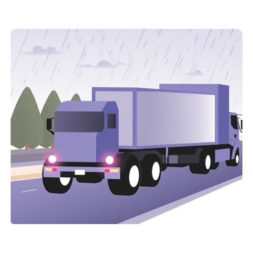 A transport truck driving on a rainy highway. The truck is large and colored in bright blue, with a shiny silver trailer attached. Rain is falling steadily, creating small puddles on the asphalt road and causing the truck's tires to splash water as it moves. Dark gray clouds fill the sky, adding to the wet atmosphere. There are faint reflections of the truck on the wet road. In the background, blurred green trees line the sides of the highway, while the rear lights of the truck illuminate the rain-soaked surroundings.