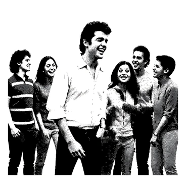 Elvis Presley is standing in a casual setting, wearing a simple shirt and jeans. He has a broad smile on his face, showcasing his enjoyment as he laughs. His hair is styled in its iconic way. Around him, a group of friends is gathered, also dressed in casual attire. They are engaged in lively conversation, some leaning in closer to hear him better. The atmosphere appears relaxed and joyful, reflecting their camaraderie.