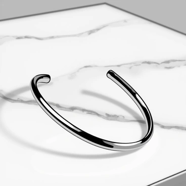 A sleek cuff bracelet made of polished silver, featuring clean lines and a smooth surface. The bracelet is gently resting on a white marble counter, showcasing its reflective quality against the subtle gray veining of the marble. The light casts soft shadows, enhancing the elegant simplicity of the bracelet and the texture of the counter beneath it.